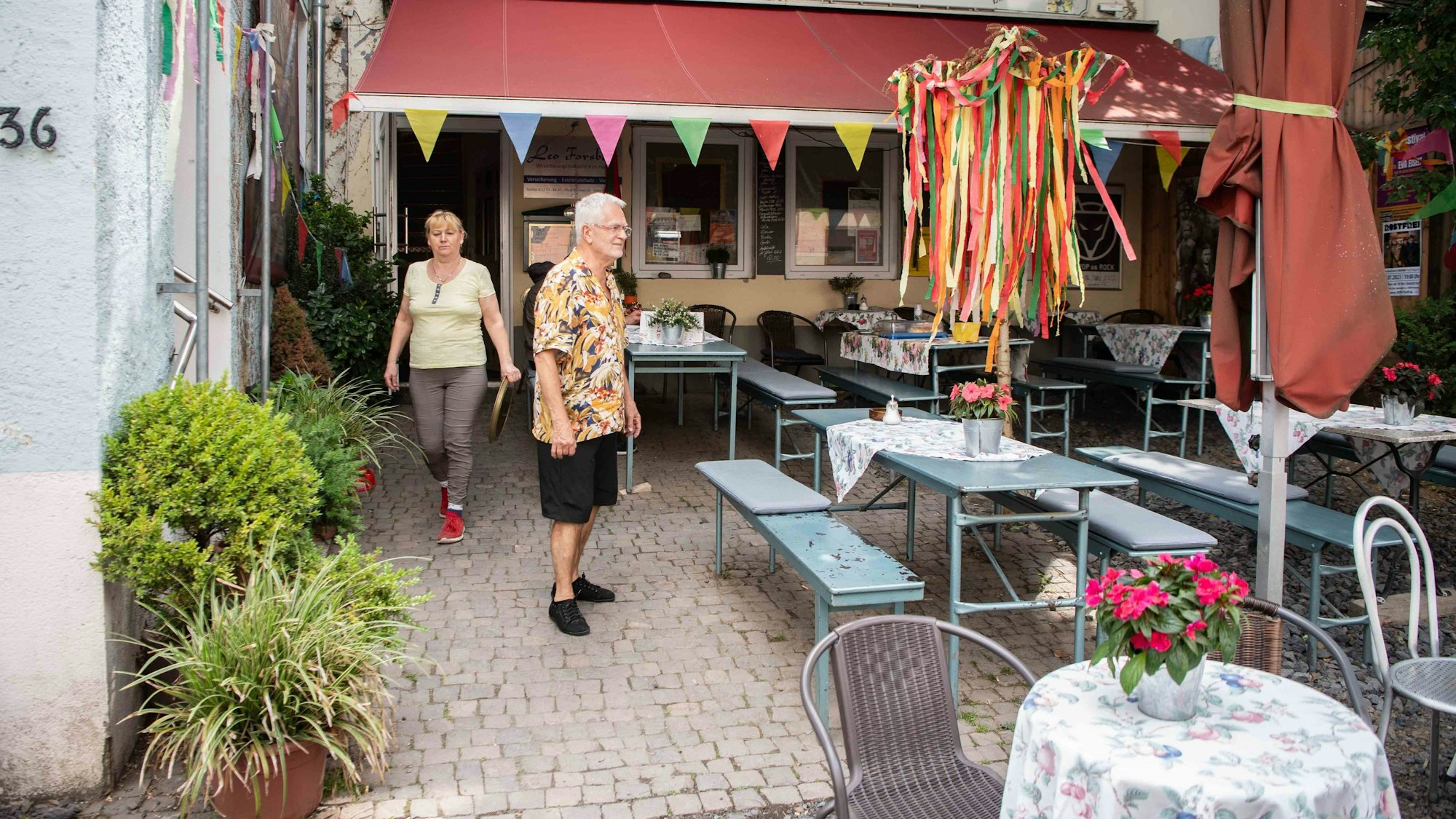 Ein Mann und eine Frau stehen im Hof eines Cafés. Ein Maibaum ist auch im Juli zur Dekoration angebracht.