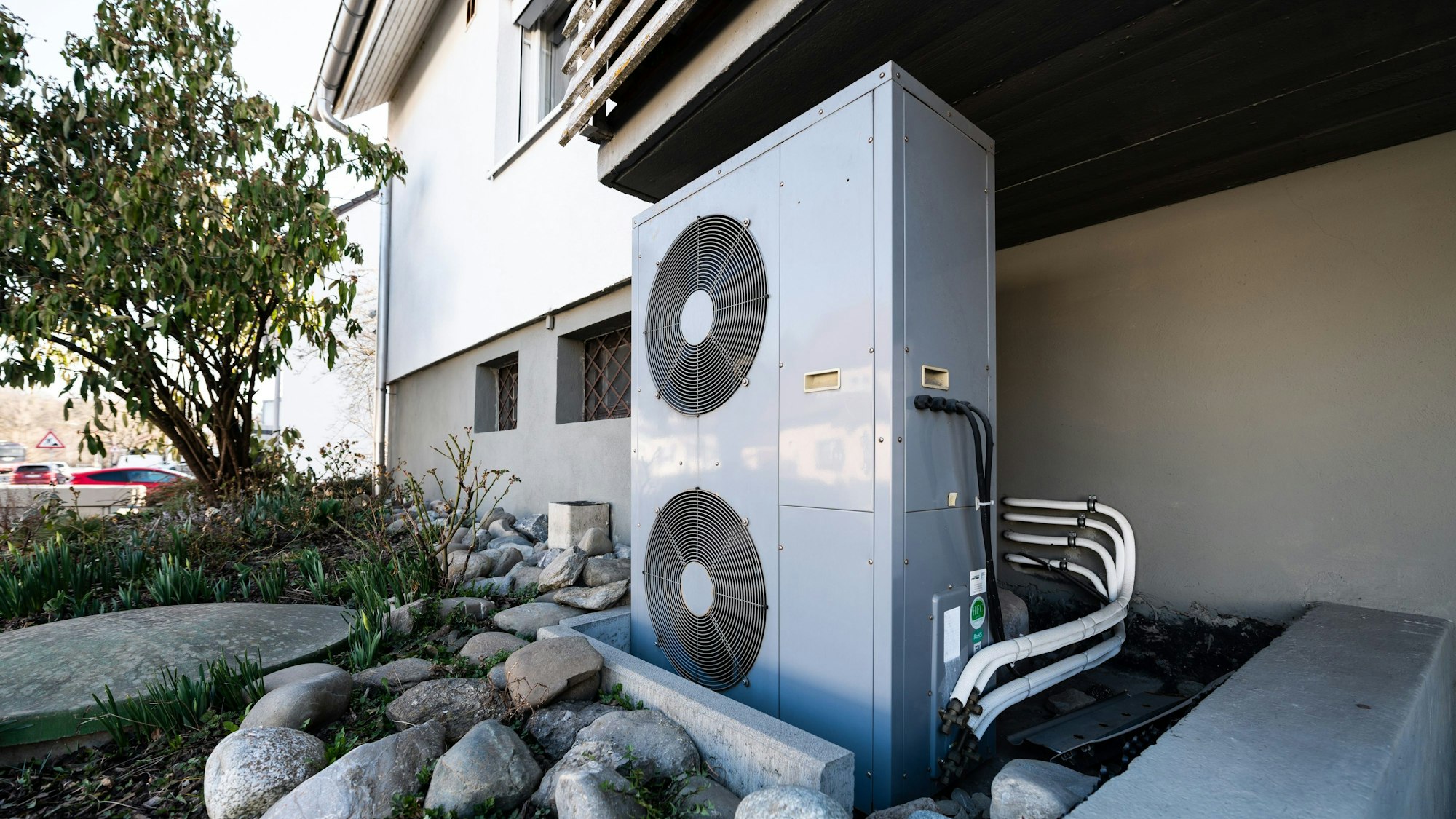 Eine Wärmepumpe steht an einem sonnigen Tag im Schatten neben einem Haus.