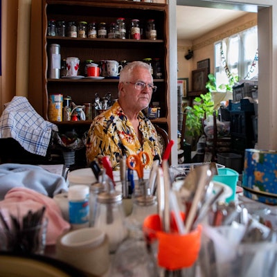 Ein Mann sitzt an einem Tisch. Darauf sind unscharf zahlreiche Dinge zu sehen, die er nach der Flut aus seinem Café gerettet hat.