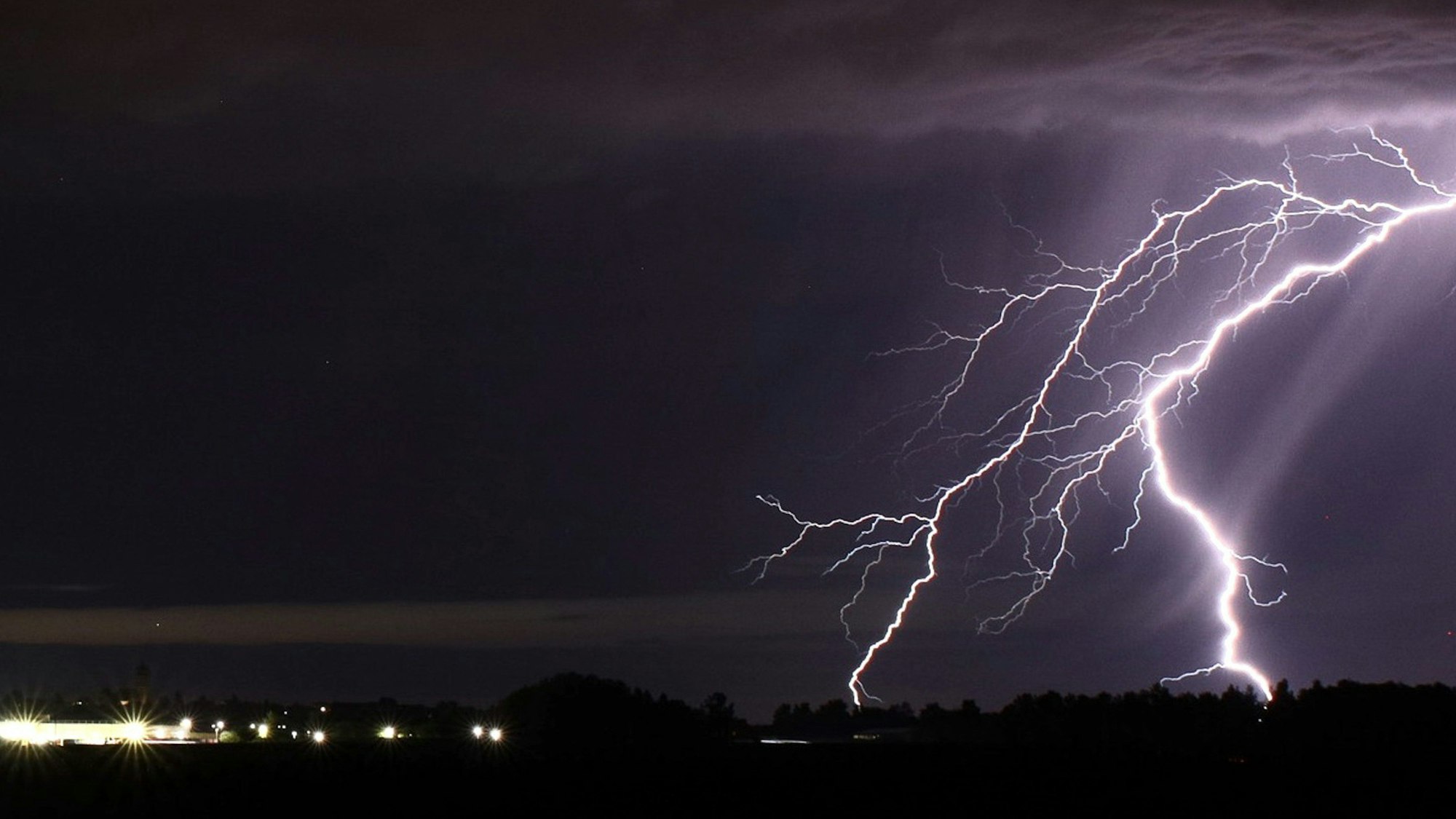 Ein starker Blitz zuckt am Nachthimmel und färbt diesen teilweise lila. (Symbolbild)