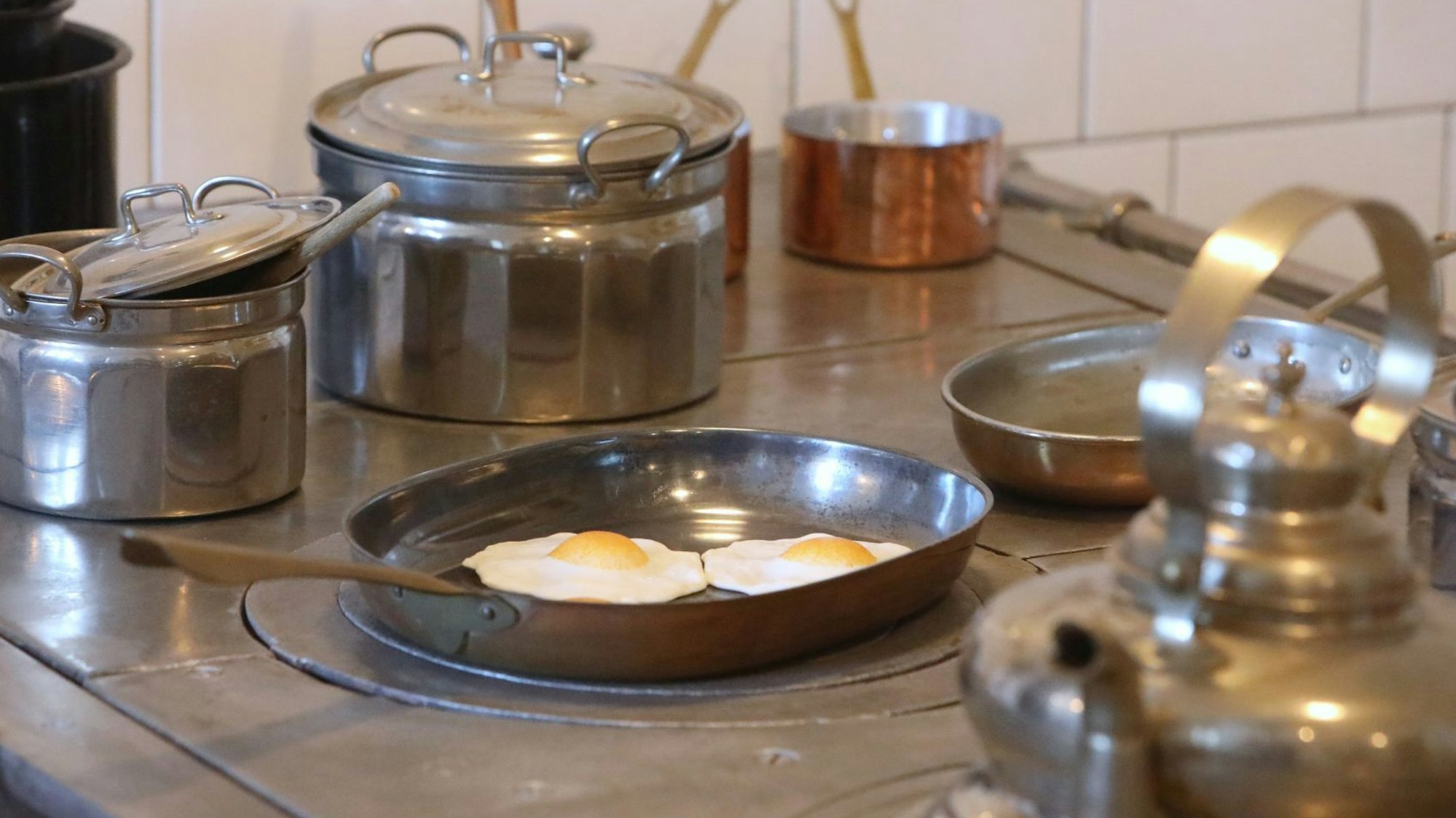Silberne und kupferne Töpfe, eine alte Bratpfanne mit unechten Spiegeleiern und ein Kessel stehen auf einem alten Herd.