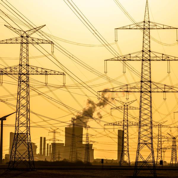 Das Foto zeigt Windräder und Strommasten bei Sonnenuntergang vor dem Braunkohlekraftwerk Niederaußem der RWE Power AG.