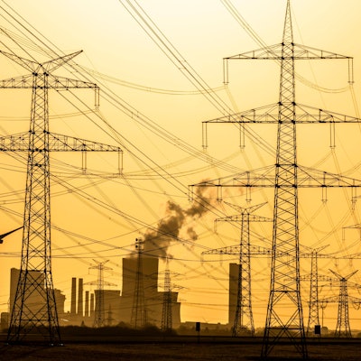 Das Foto zeigt Windräder und Strommasten bei Sonnenuntergang vor dem Braunkohlekraftwerk Niederaußem der RWE Power AG.