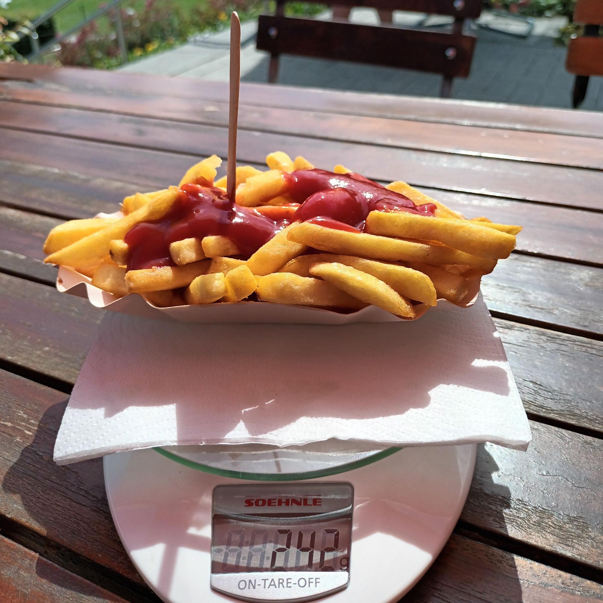 Ein Schälchen goldgelber Pommes mit Ketchup steht auf einer Küchenwaage, die 242 Gramm anzeigt.