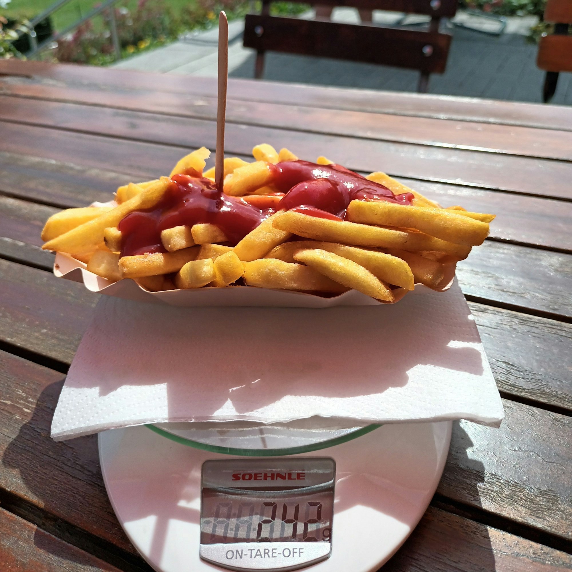 Ein Schälchen goldgelber Pommes mit Ketchup steht auf einer Küchenwaage, die 242 Gramm anzeigt.