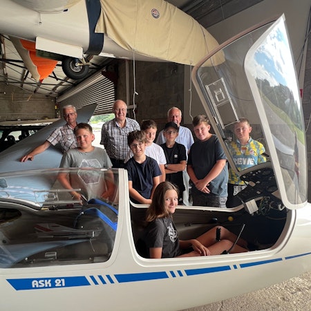 Kinder und Erwachsene haben sich rund um ein Segelflugzeug in einem Hangar am Flugplatz Neye aufgestellt.