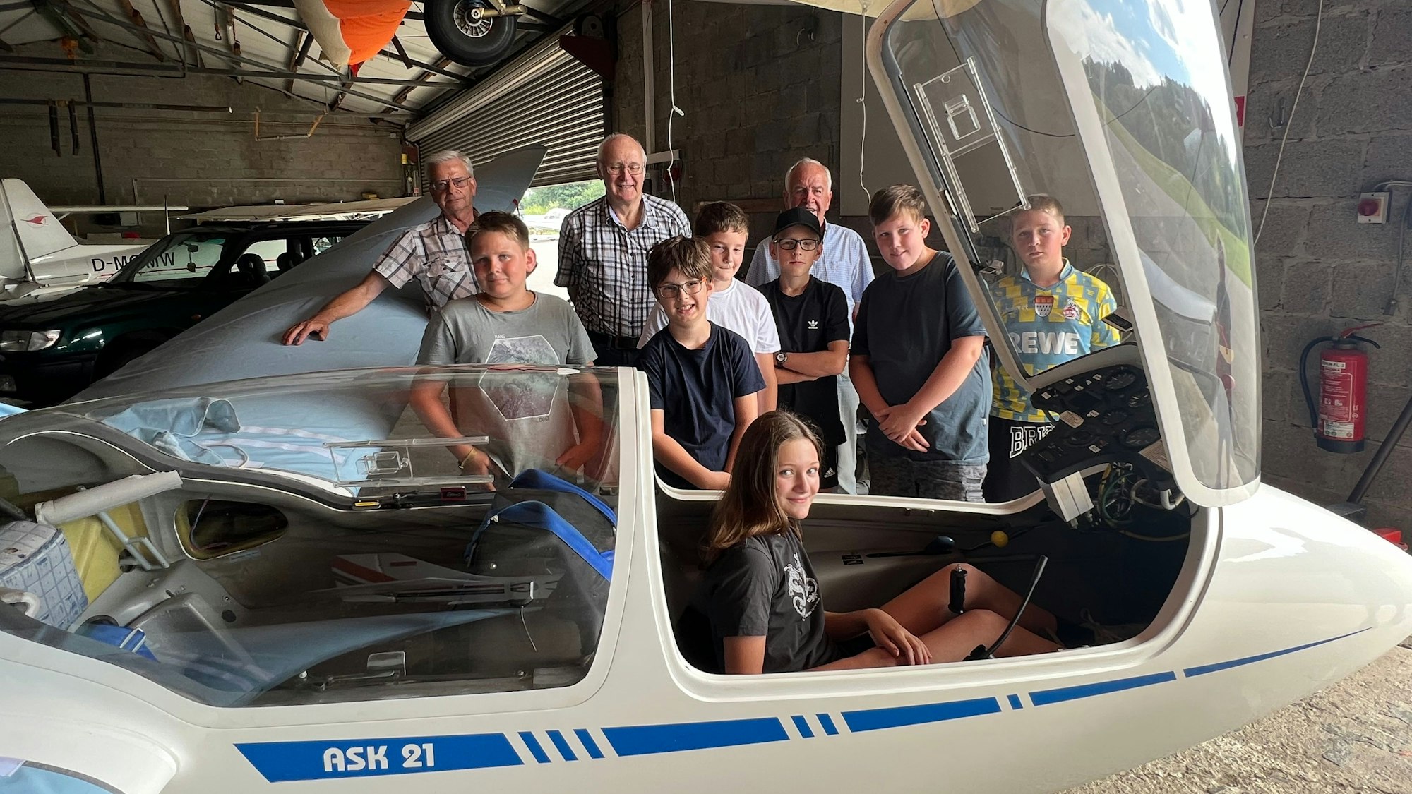 Kinder und Erwachsene haben sich rund um ein Segelflugzeug in einem Hangar am Flugplatz Neye aufgestellt.