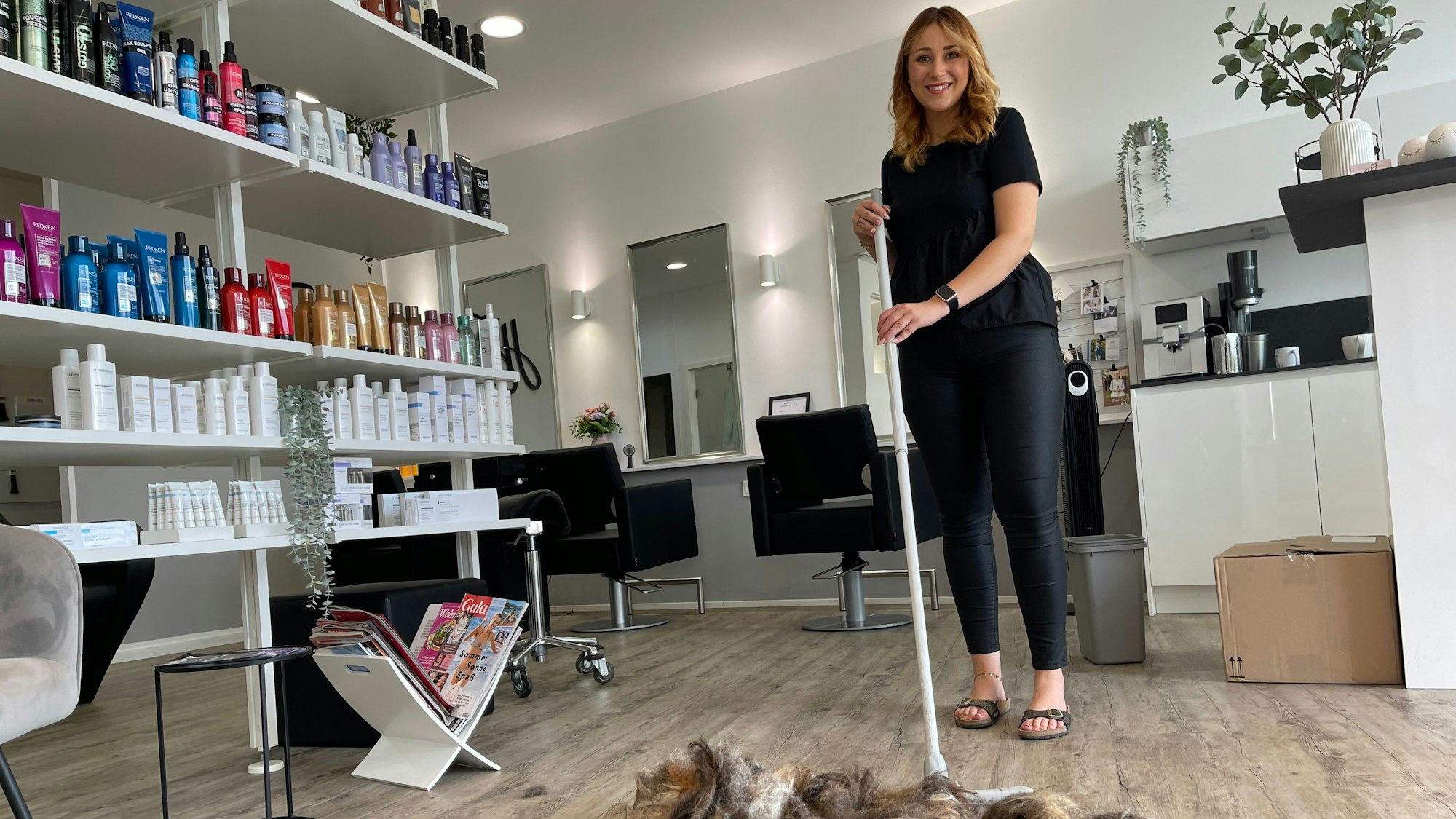 Friseurin Helena Friedrich aus Königswinter-Oberpleis, eine elegante junge Frau, fegt in ihrem Friseursalon Haare zusammen.