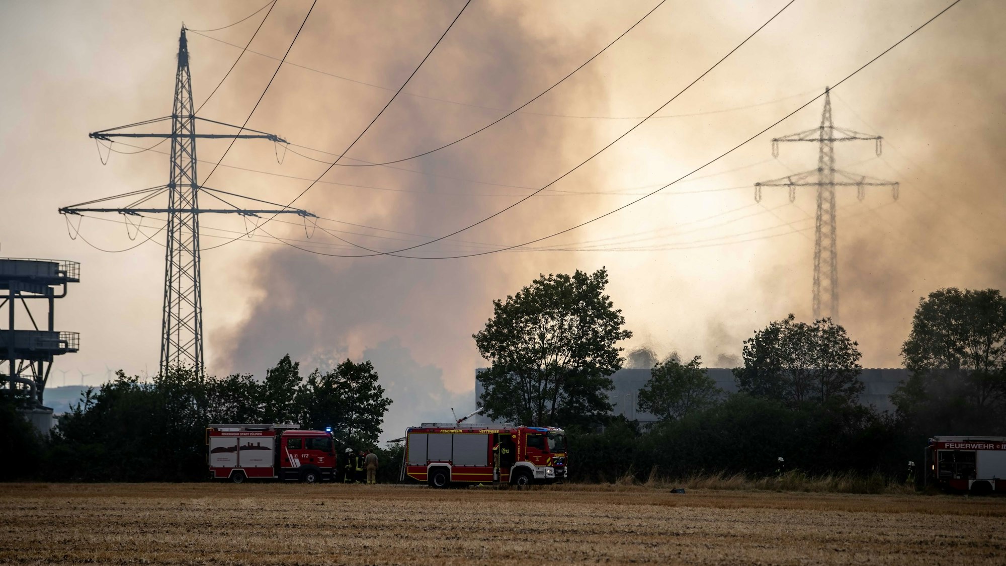 Drei Feuerwehrfahrzeuge stehen auf einem Feldweg. Im Hintergrund ist Qualm und die Oberleitung zu sehen, die den Feuerwehrleuten Sorge bereitete.