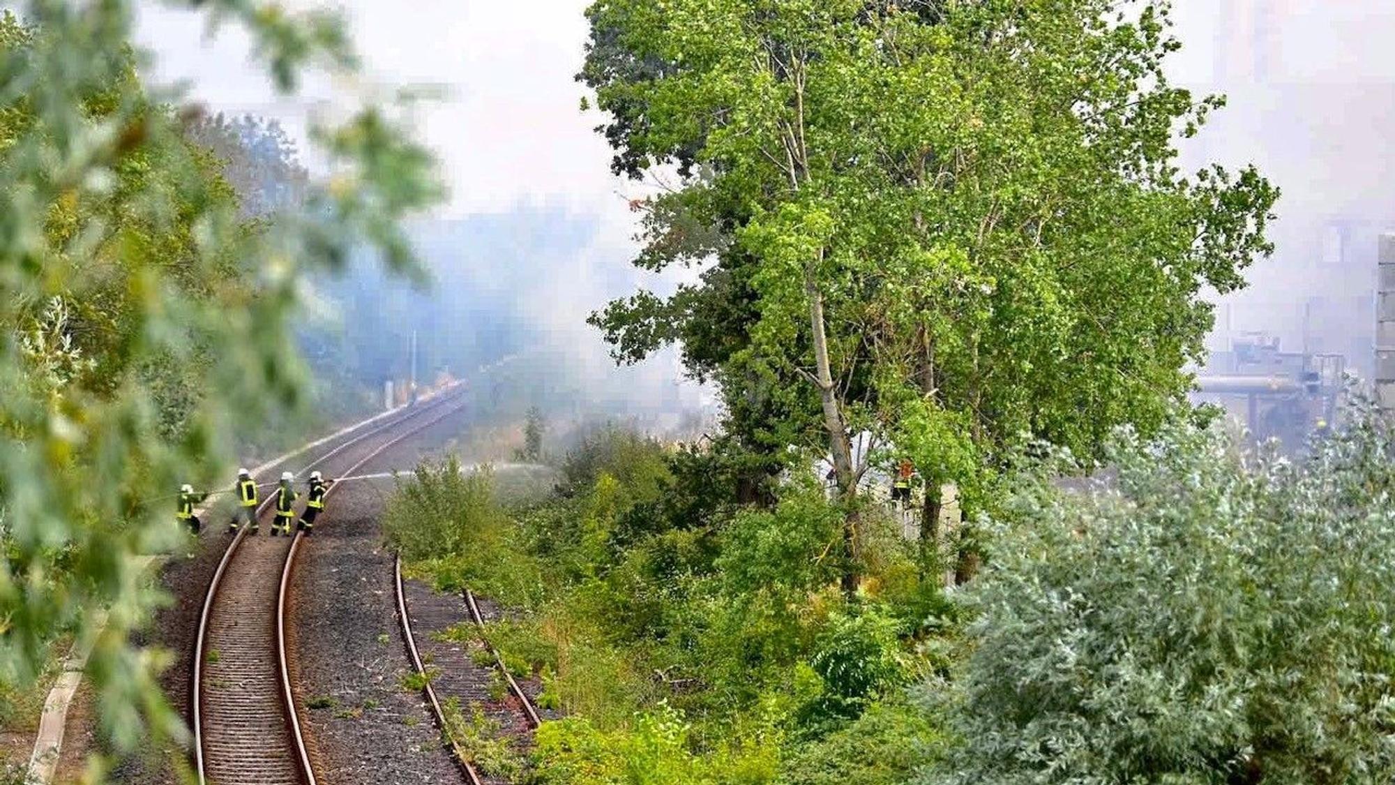 Feuerwehrleute nehmen auf den Gleisen ein Strahlrohr vor, um die angrenzende Böschung zu schützen.