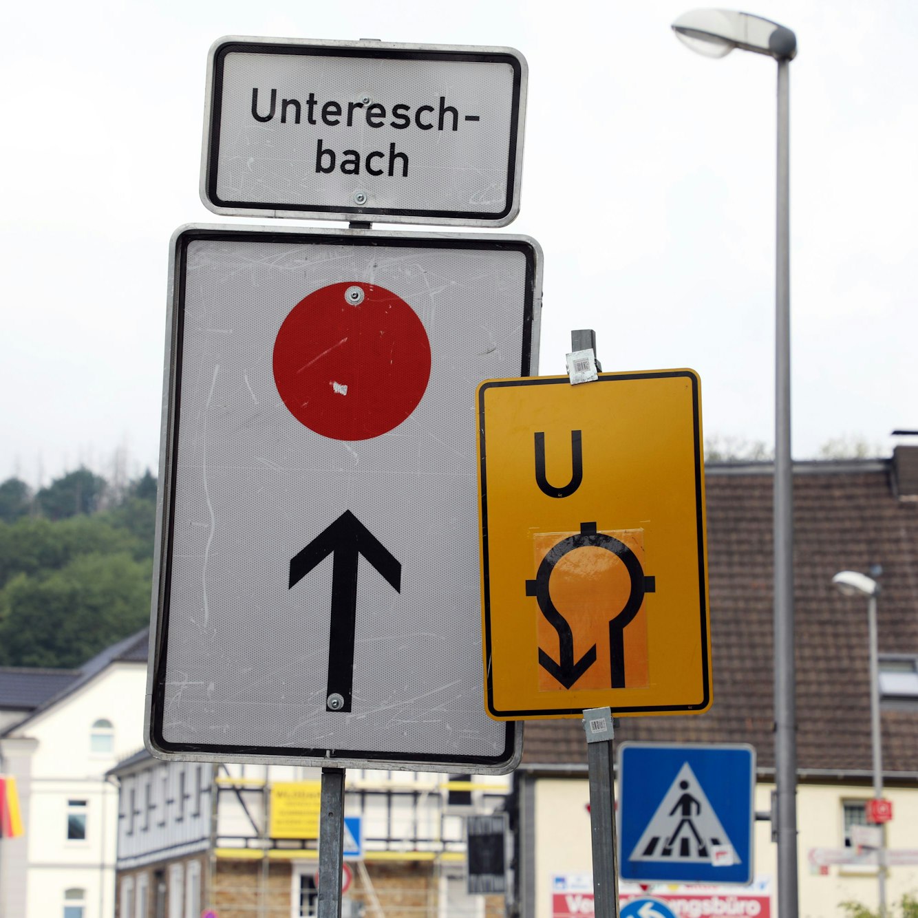 Zwei Umleitungsschilder stehen nebeneinander vor einem Kreisverkehr. Ein Pfeil weist nach geradeaus Richtung Untereschbach, ein weitere durch den Kreisverkehr zurück.