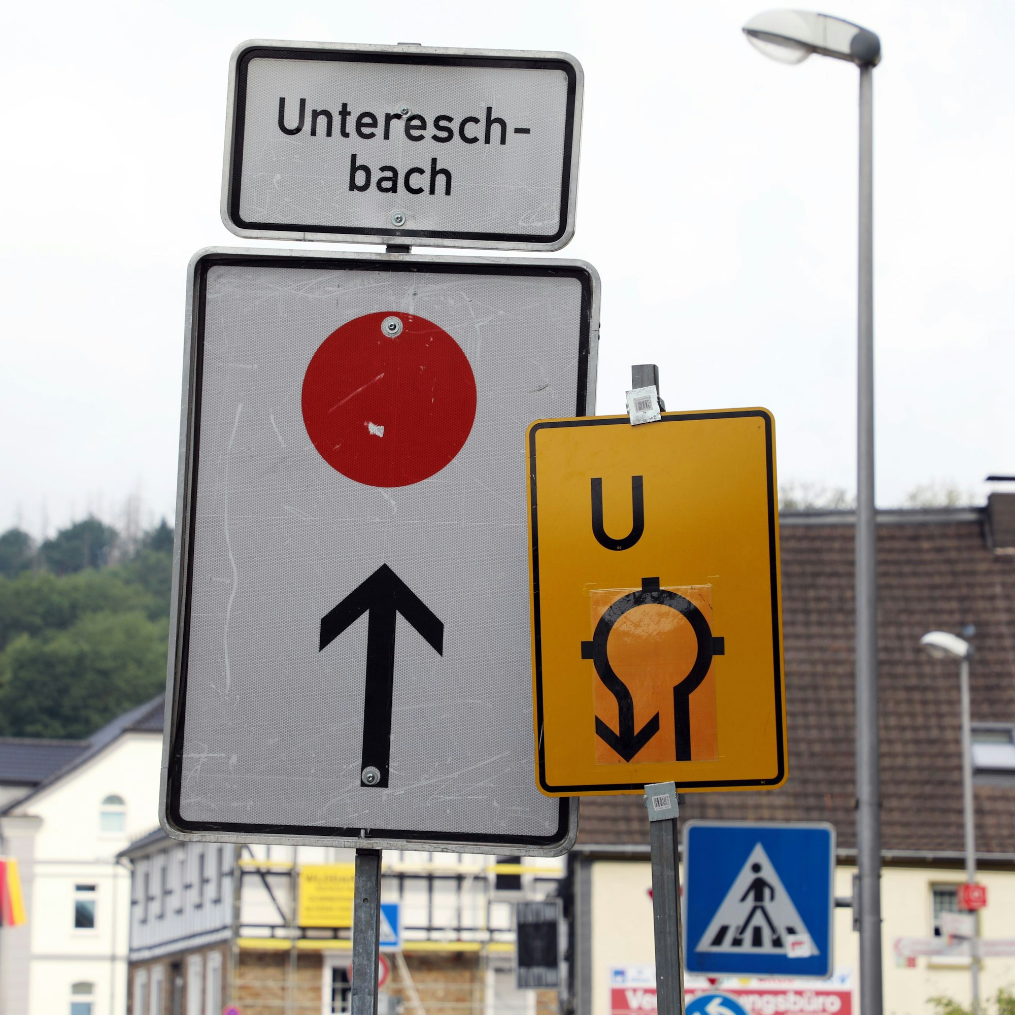 Zwei Umleitungsschilder stehen nebeneinander vor einem Kreisverkehr. Ein Pfeil weist nach geradeaus Richtung Untereschbach, ein weitere durch den Kreisverkehr zurück.