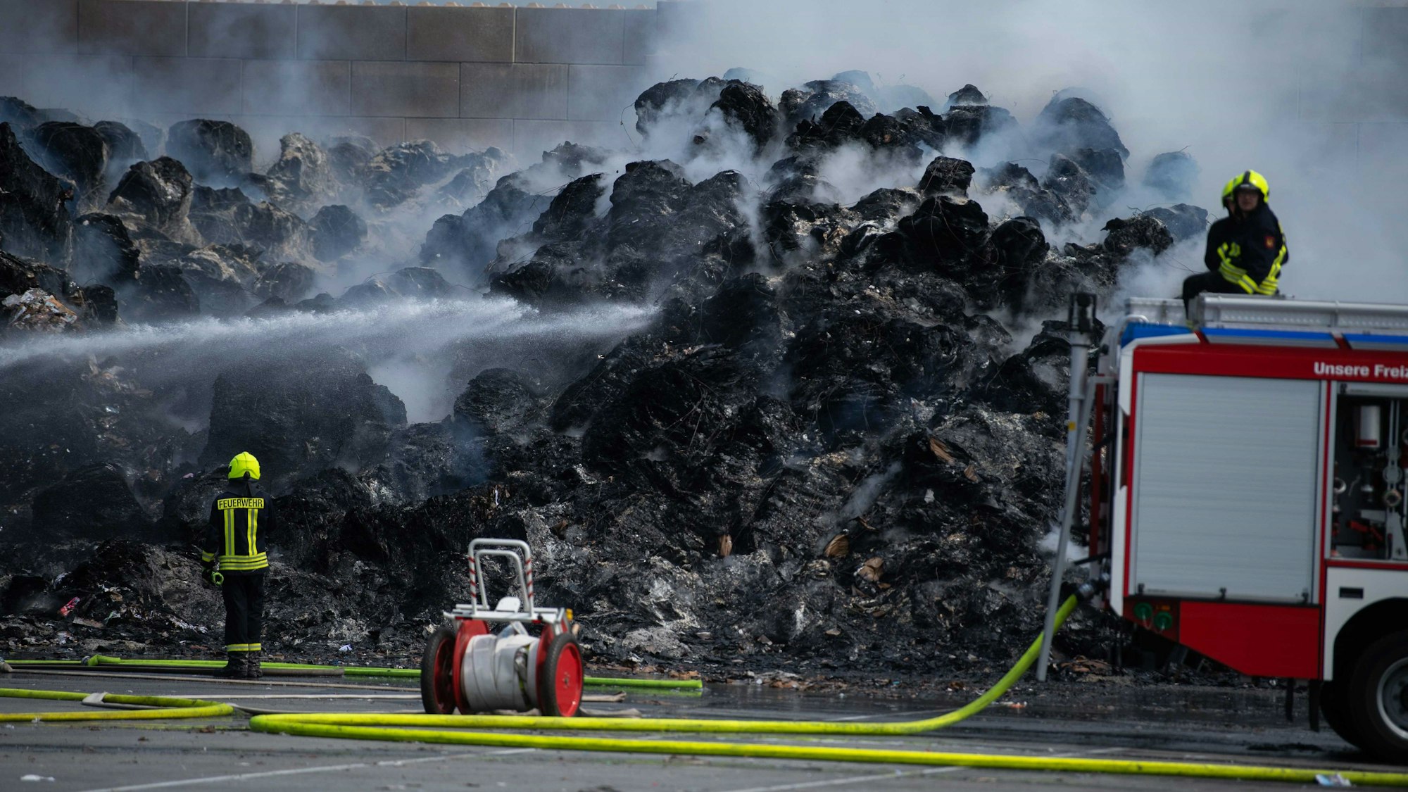 Feuerwehrleute löschen die brennenden Papierballen.