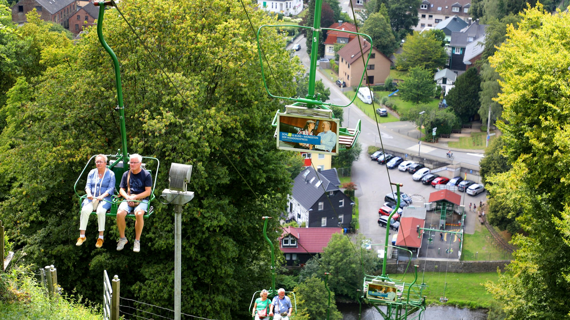 Blick ins Tal: Menschen fahren mit einem Sessellift von der Talstation am Ufer der Wupper den Berg hinauf.