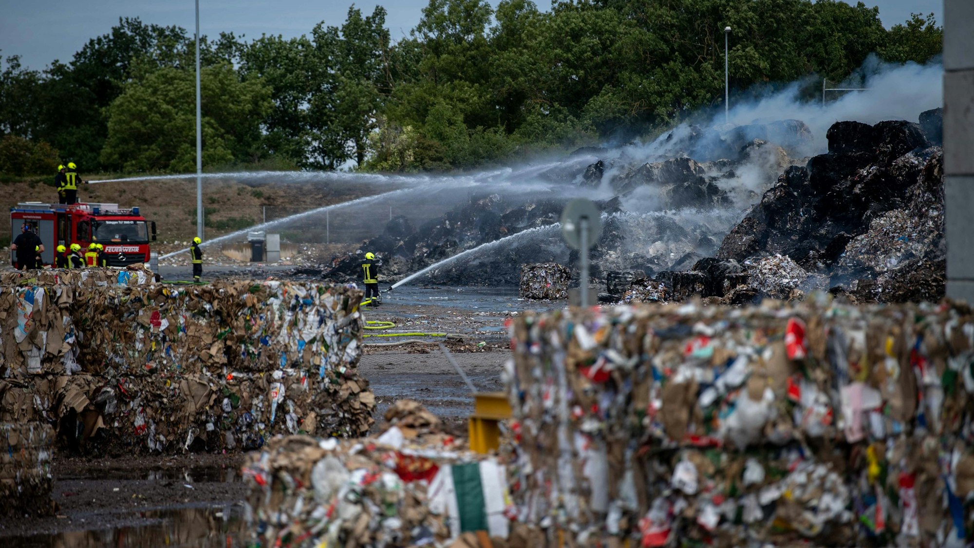 Das Bild zeigt Altpapierballen, die auf dem Gelände von Smurfit Kappa in Brand geraten sind. Die Feuerwehr löscht aus zahlreichen Strahlrohren.