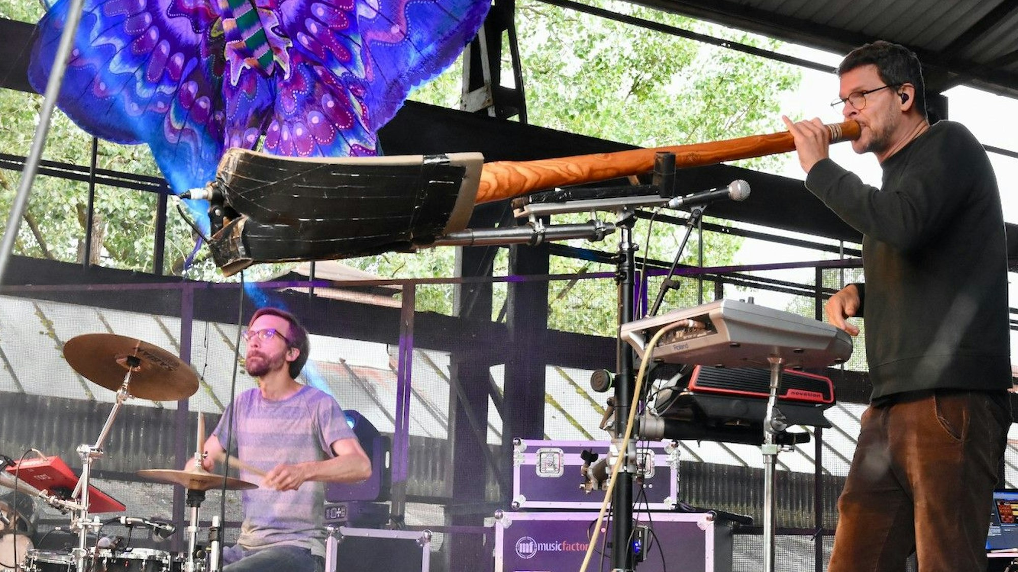 Zwei Männer stehen auf einer Bühne, einer spielt Schlagzeug, der andere ein Didgeridoo.