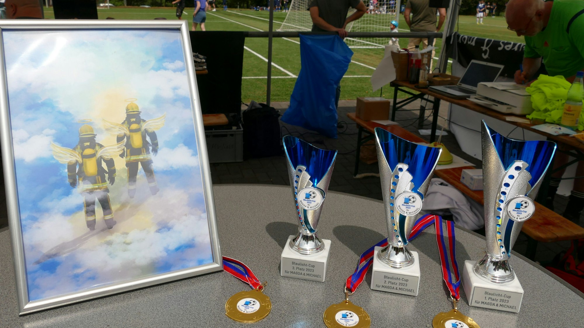 Drei Pokale stehen auf einem Tisch neben einem gemalten Bild.