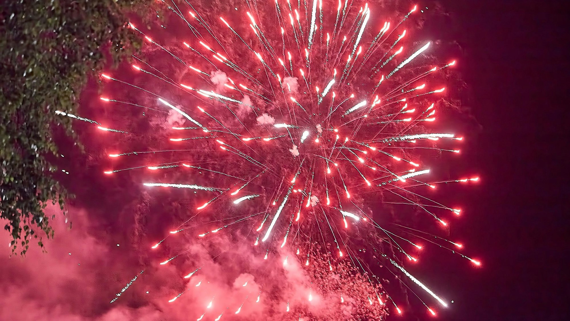 Ein roter Funkenregen explodierender Feuerwerksraketen erleuchtet den Nachthimmel.