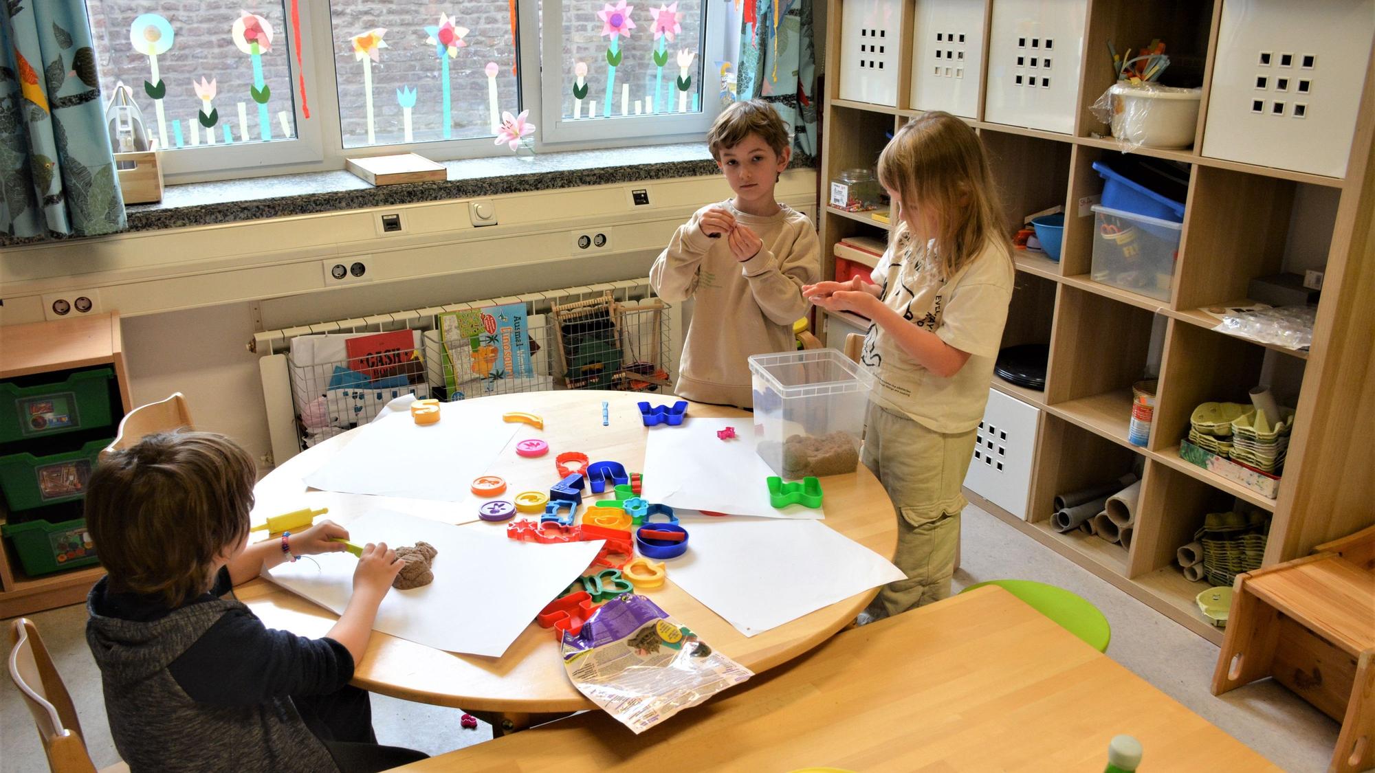 Drei Kinder stehen an einem Tisch und basteln.