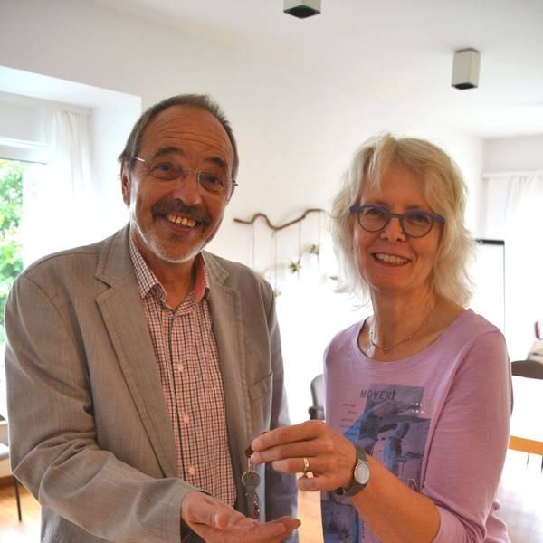 Ein Mann und eine Frau stehen nebeneinander. Sie übergibt ihm einen Schlüssel.