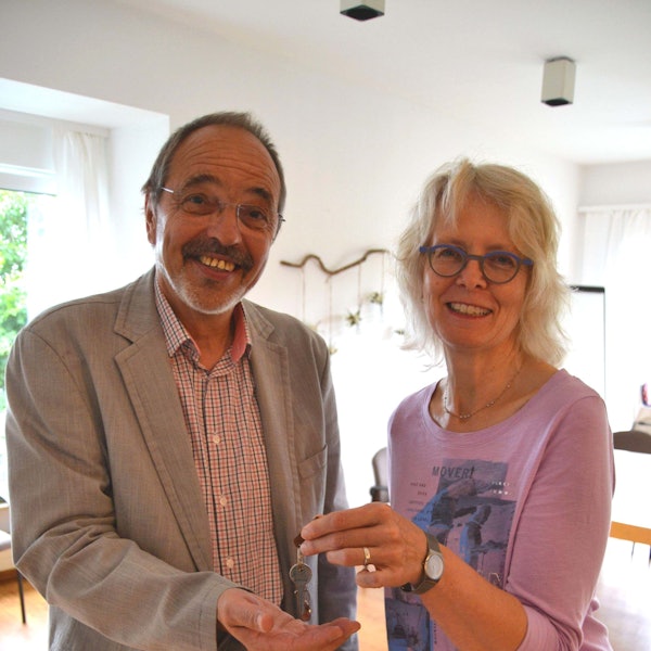 Ein Mann und eine Frau stehen nebeneinander. Sie übergibt ihm einen Schlüssel.