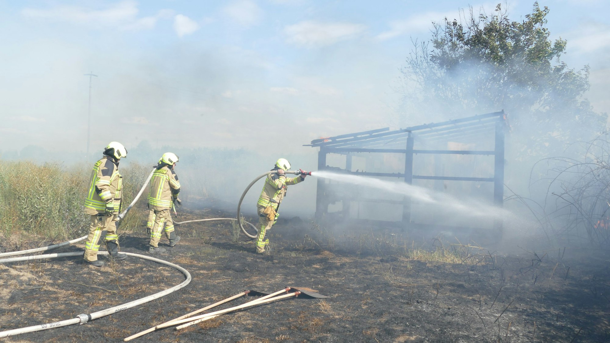 Feuerwehrleute halten einen Löschschlauch, der Wasser auf ein abgebranntes Gartencenter schießt.