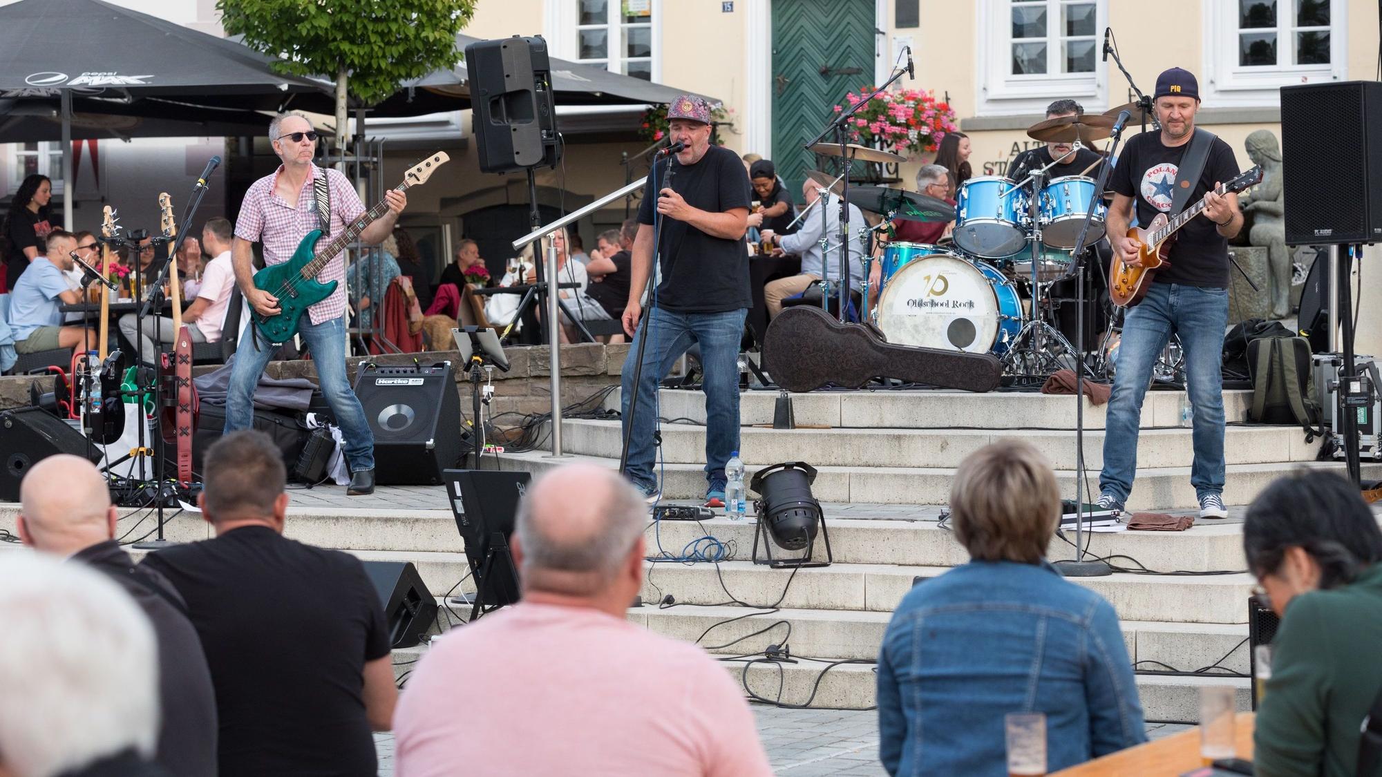 Eine Band spielt auf Treppen in einem Stadtzentrum vor Publikum.