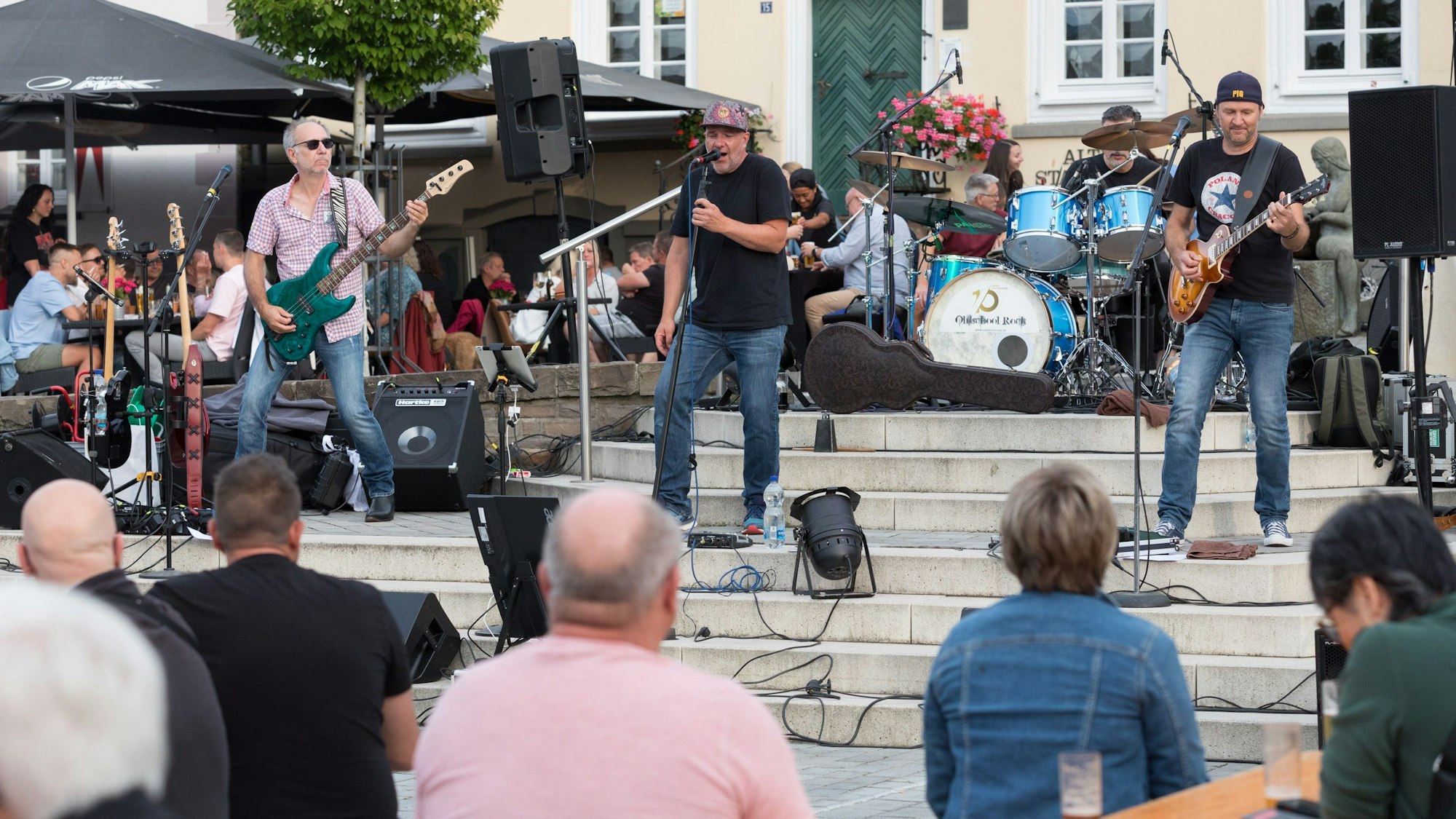 Eine Band spielt auf Treppen in einem Stadtzentrum vor Publikum.