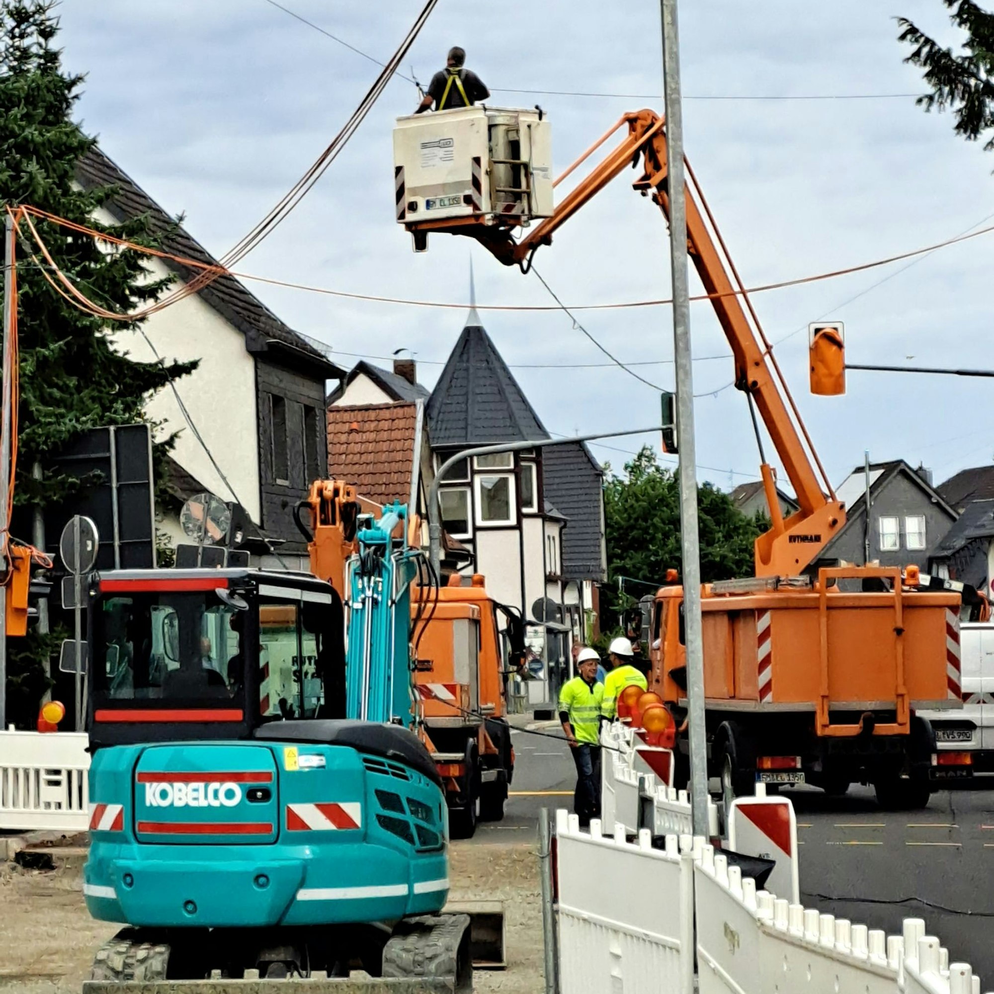 Warnbaken sperren eine Baustelle ab, dahinter steht ein Hubwagen, in dem ein Arbeiter Seile über der Straße demontiert.