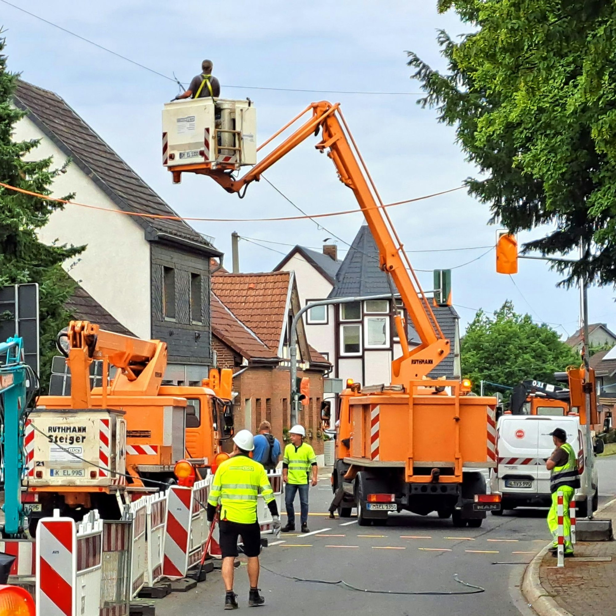 Monteure stehen auf einer Straße, von Hubsteigern aus werden Seile über der Straße abmontiert.