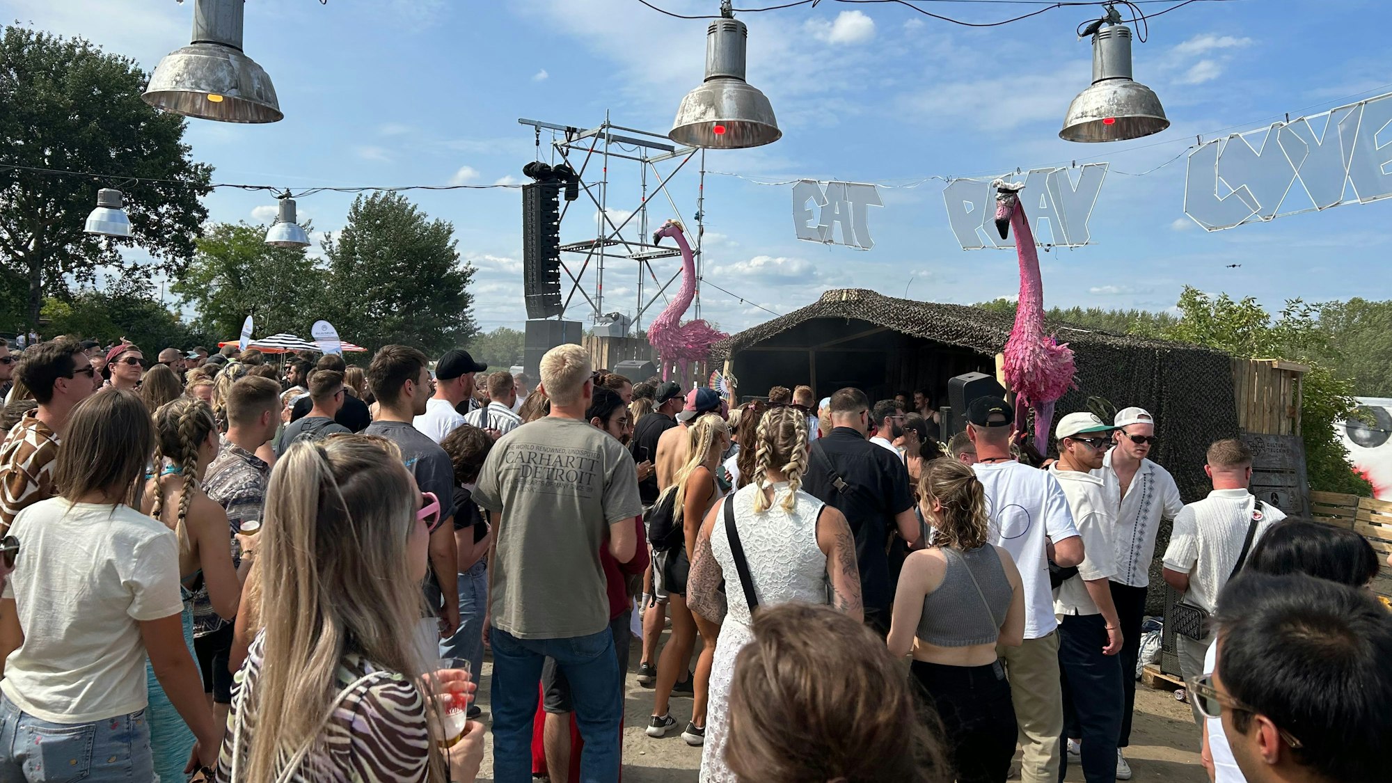 Eine Menschenmenge steht vor einem DJ-Pult unter freiem Himmel.