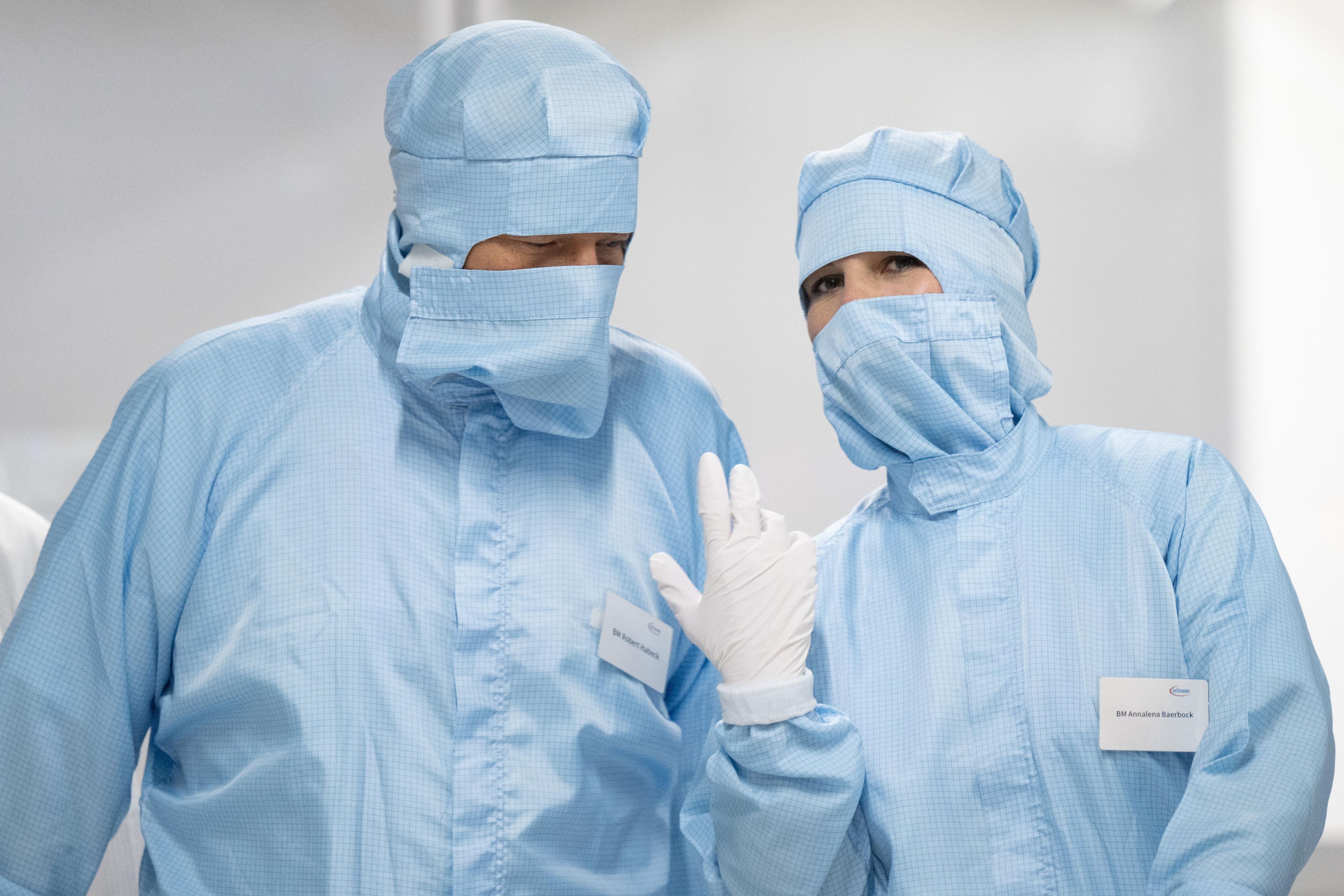 Robert Habeck und Annalena Baerbock, gekleidet in hellblaue Schutzanzüge, die nur noch die Augen freilassen.