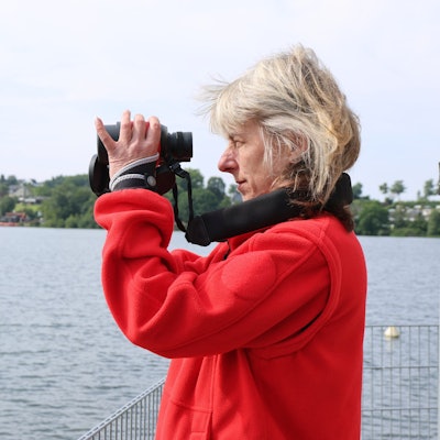 Eine Frau in rotem Fließpullover schaut durch ein Fernglas aufs Wasser.