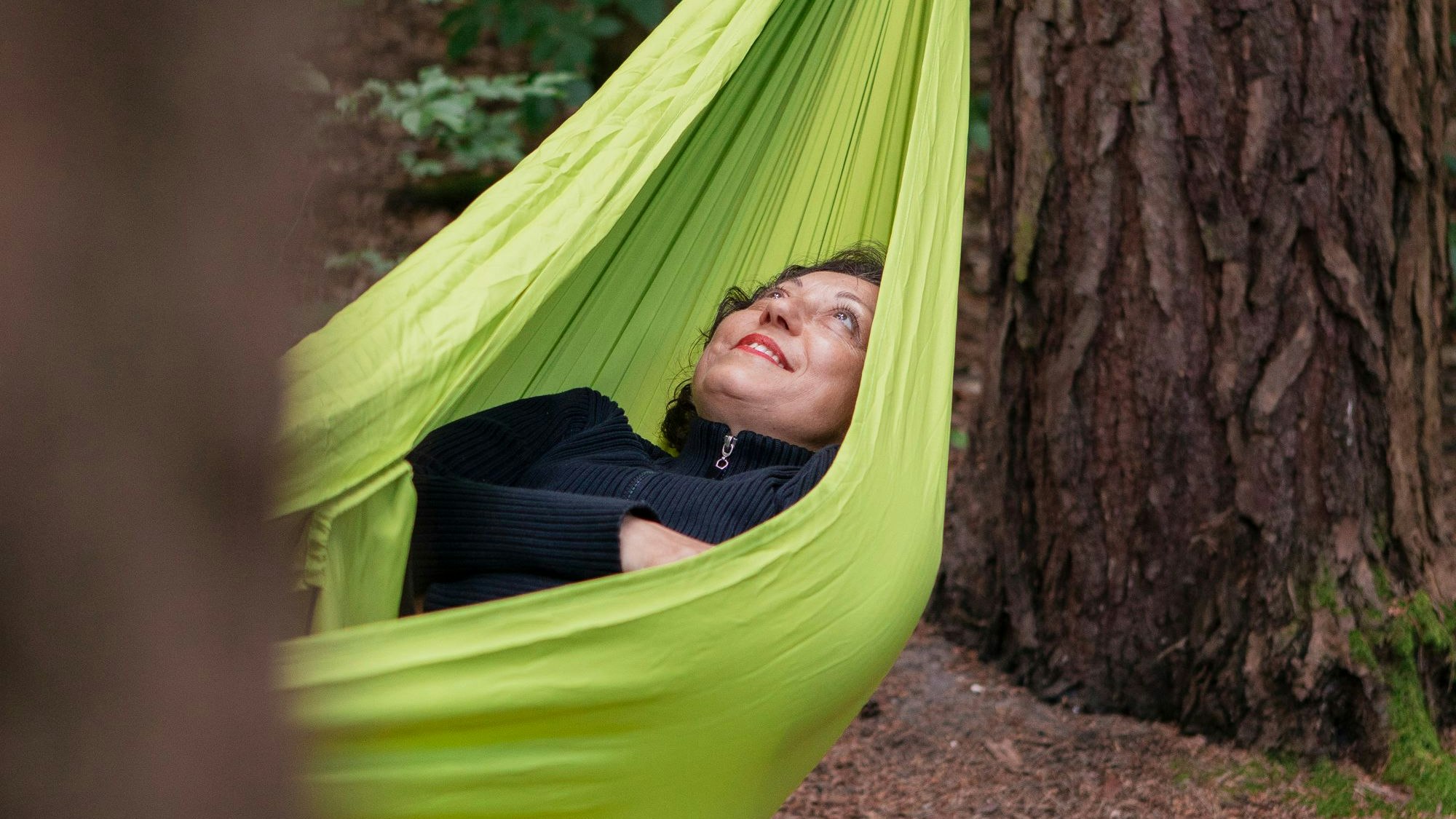 Eine Frau liegt in einer grünen Hängematte die im Wald aufgespannt ist.