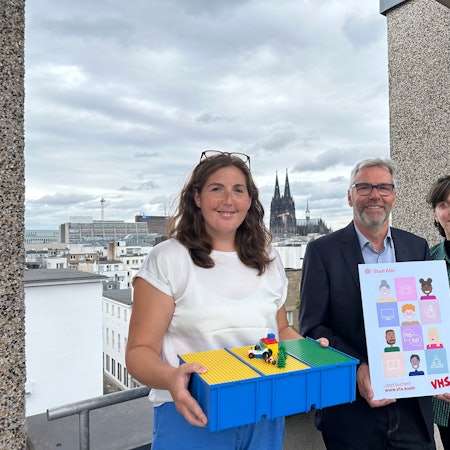 Dozentin Yvonne Romes, Leiter Jakob Schüller und Kursteilnehmerin Jana Wolf stehen auf einer Terrasse mit Blick auf den Kölner Dom.