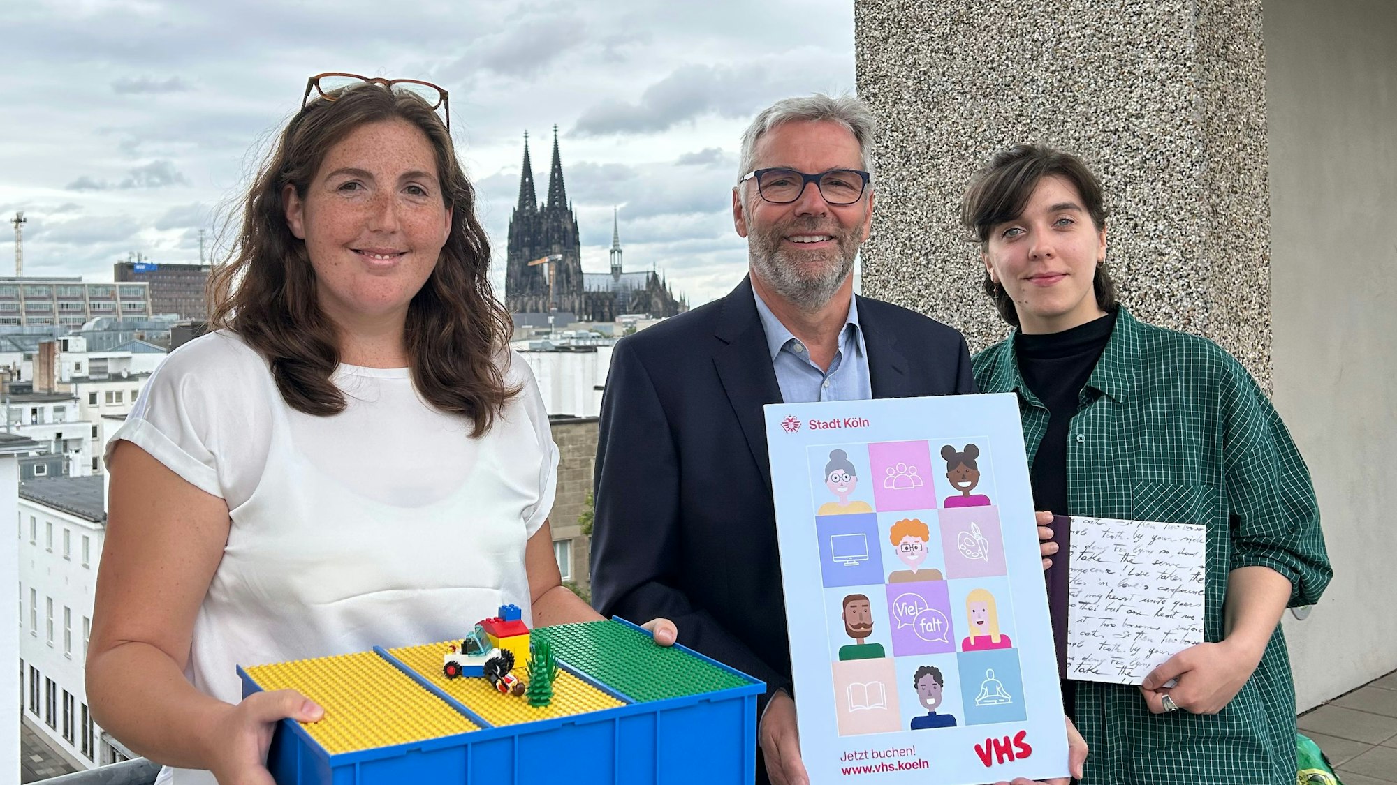 Dozentin Yvonne Romes, Leiter Jakob Schüller und Kursteilnehmerin Jana Wolf stehen auf einer Terrasse mit Blick auf den Kölner Dom.