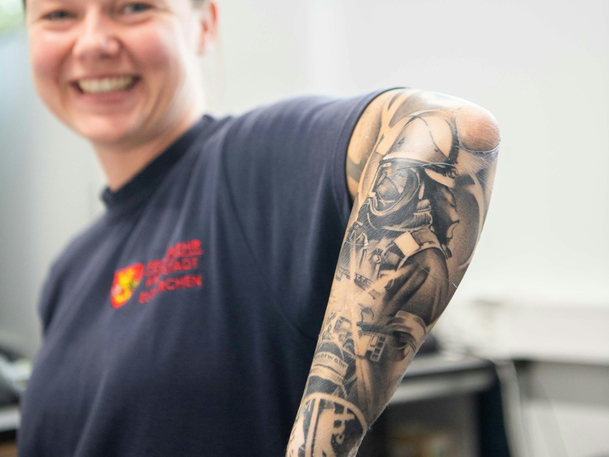 Eine Frau zeigt ihren linken Unterarm, den zahlreiche Tattoos mit Feuerwehr-Motiven zieren.