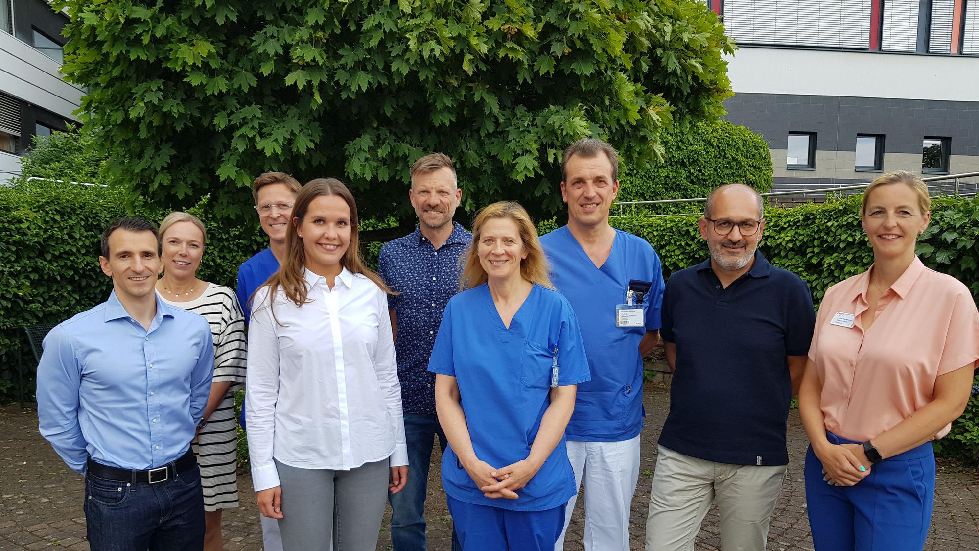Das ärztliche Kernteam steht vor einer Hecke.