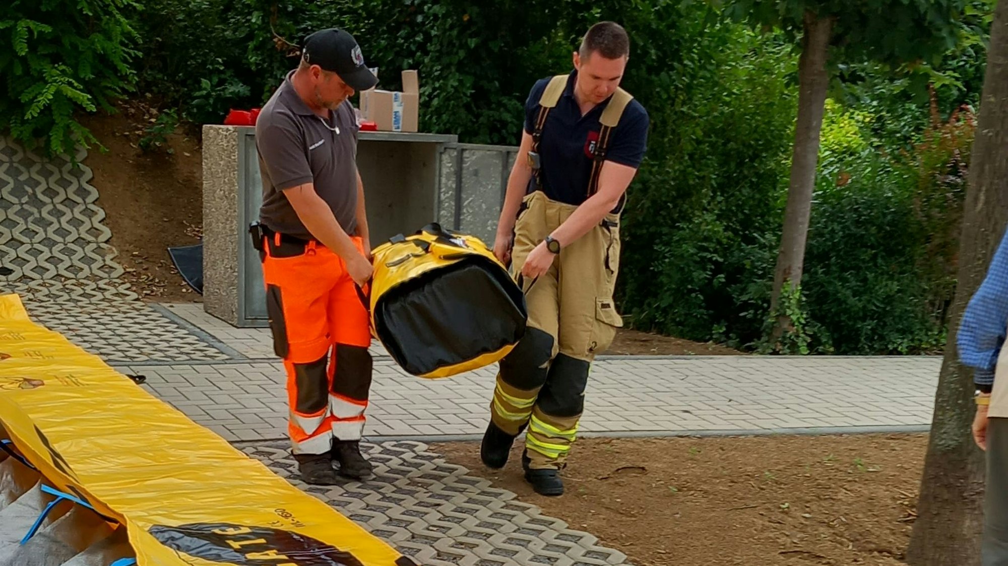 24.7.2023 Zwei Helfer tragen einen Teil der Hochwasserbarriere für das Rodderfeld in Rheinbach