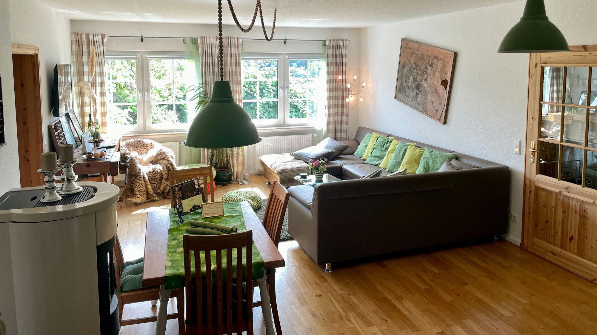 Blick in eine Ferienwohnung: Durch die Fenster ist grüne Landschaft zu sehen.