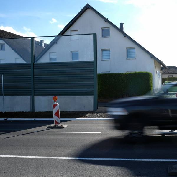 Das Foto zeigt einen Pick-up, der auf einer zweispurigen Straße an Häusern vorbeifährt.