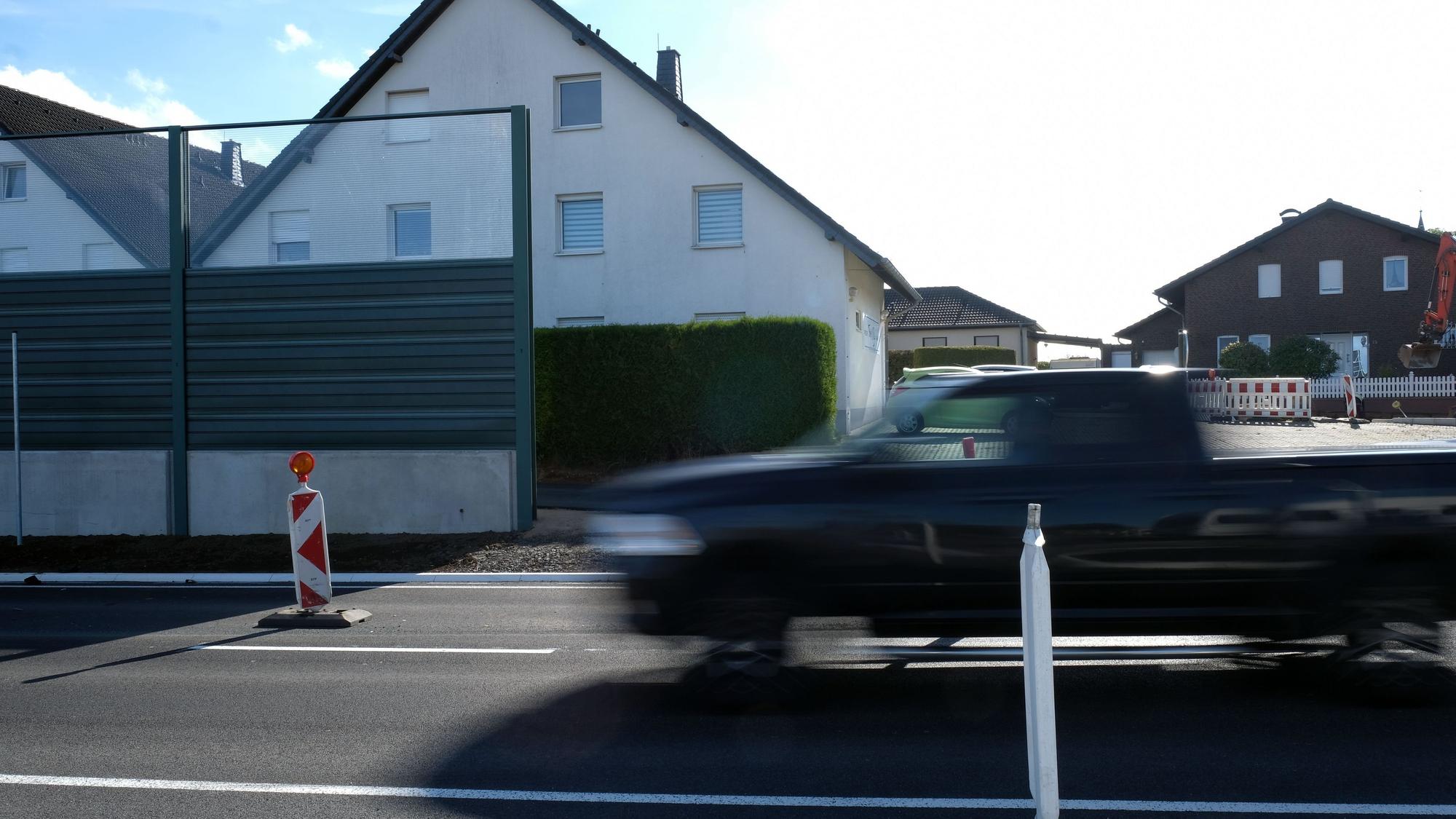 Das Foto zeigt einen Pick-up, der auf einer zweispurigen Straße an Häusern vorbeifährt.