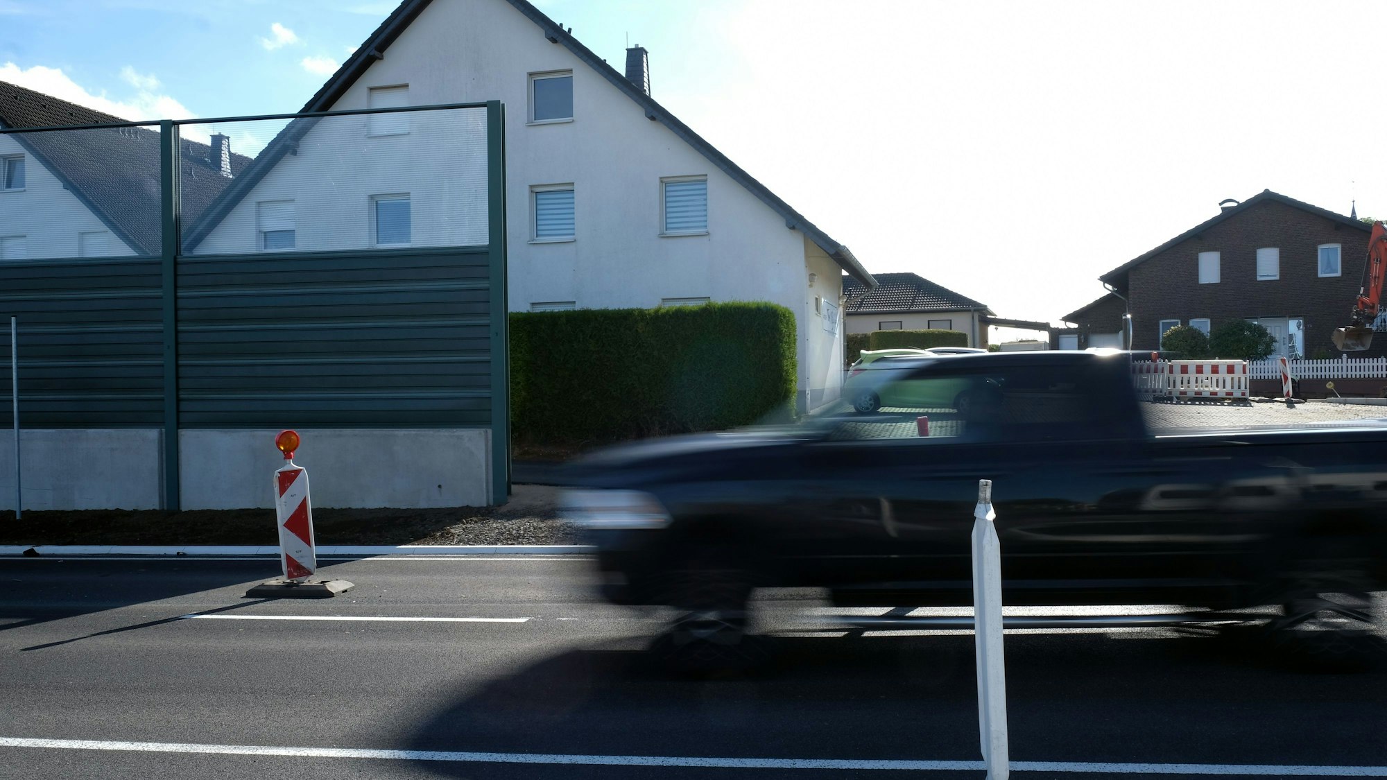 Das Foto zeigt einen Pick-up, der auf einer zweispurigen Straße an Häusern vorbeifährt.
