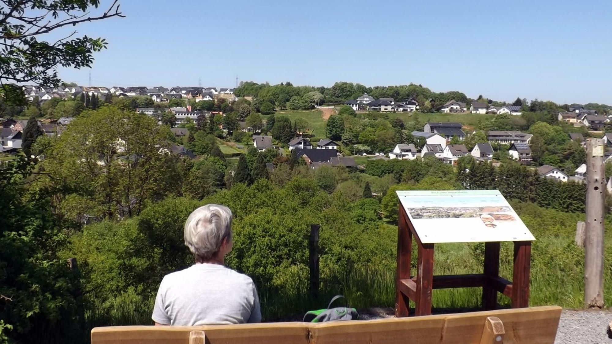 Eine Frau sitzt auf einer Bank mit Aussicht auf ein idyllisches Dorf