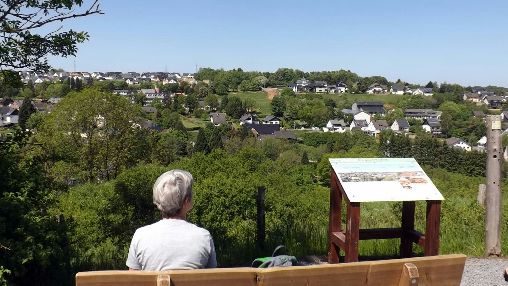 Eine Frau sitzt auf einer Bank mit Aussicht auf ein idyllisches Dorf