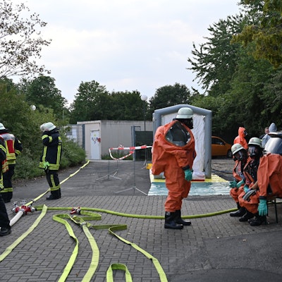 Feuerwehrleute in Schutzanzügen stehen und sitzen vor dem Bad, Schläuche sind ausgerollt.