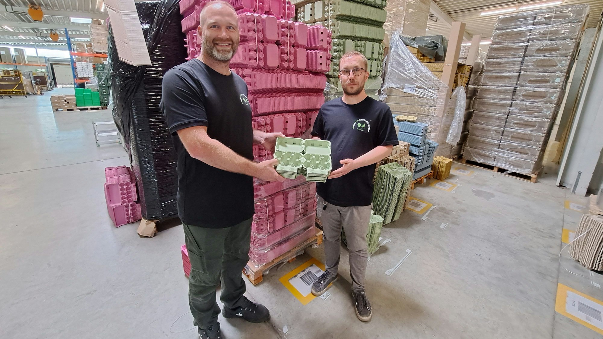 Firmengründer Meik Klose (rechts) und sein Geschäftspartner Daniel Debus stehen im Lager ihres Unternehmens eierschateln.de vor tausenden Eierkartons in unterschiedlichen Farben.