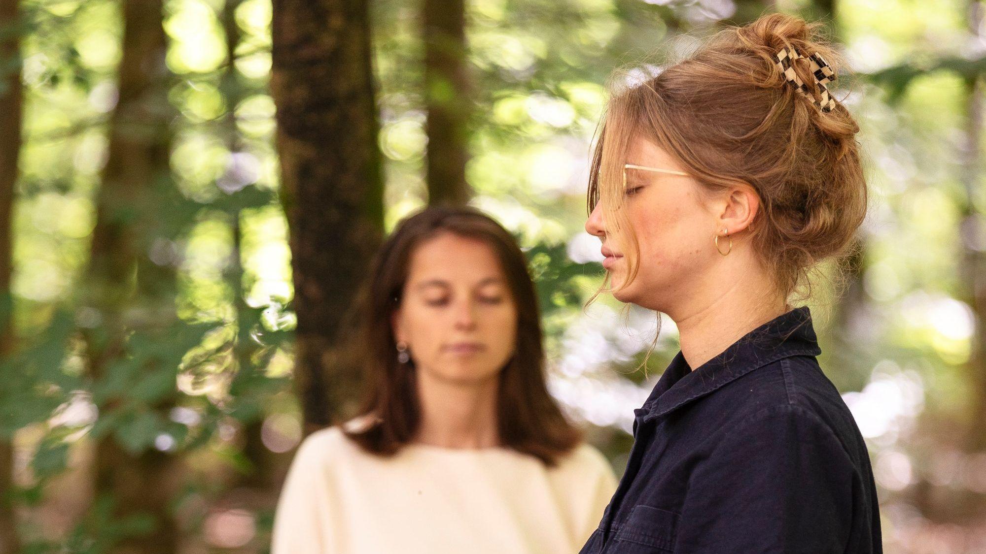 Zwei Frauen stehen mit geschlossenen Augen im Wald.