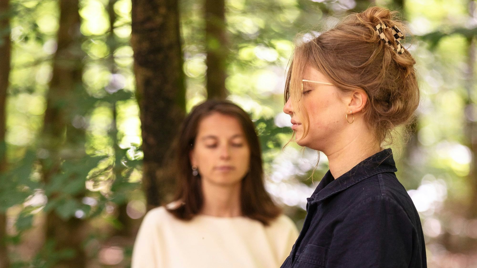 Zwei Frauen stehen mit geschlossenen Augen im Wald.