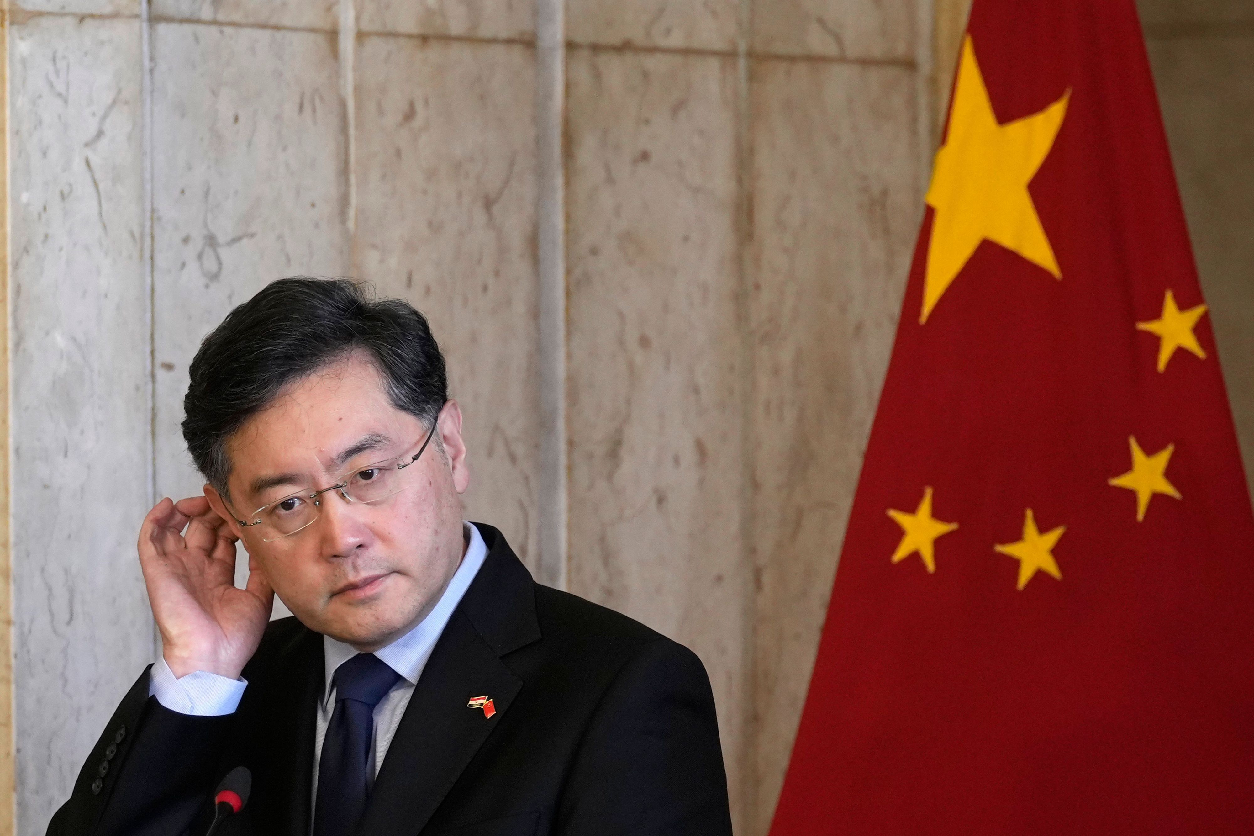 Der verschwundene ehemalige Außenminister von China, Qin Gang, kratz sich am Ohr - im Hintergrund ist eine chinesische Landesflagge zu sehen.